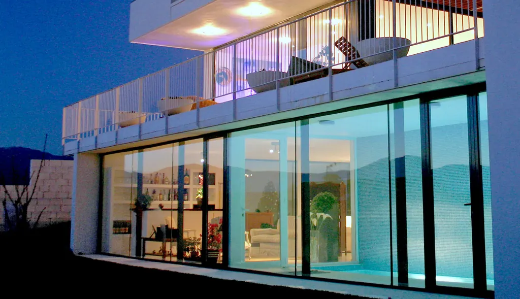 Vivienda con grandes cerramientos de aluminio iluminados al anochecer